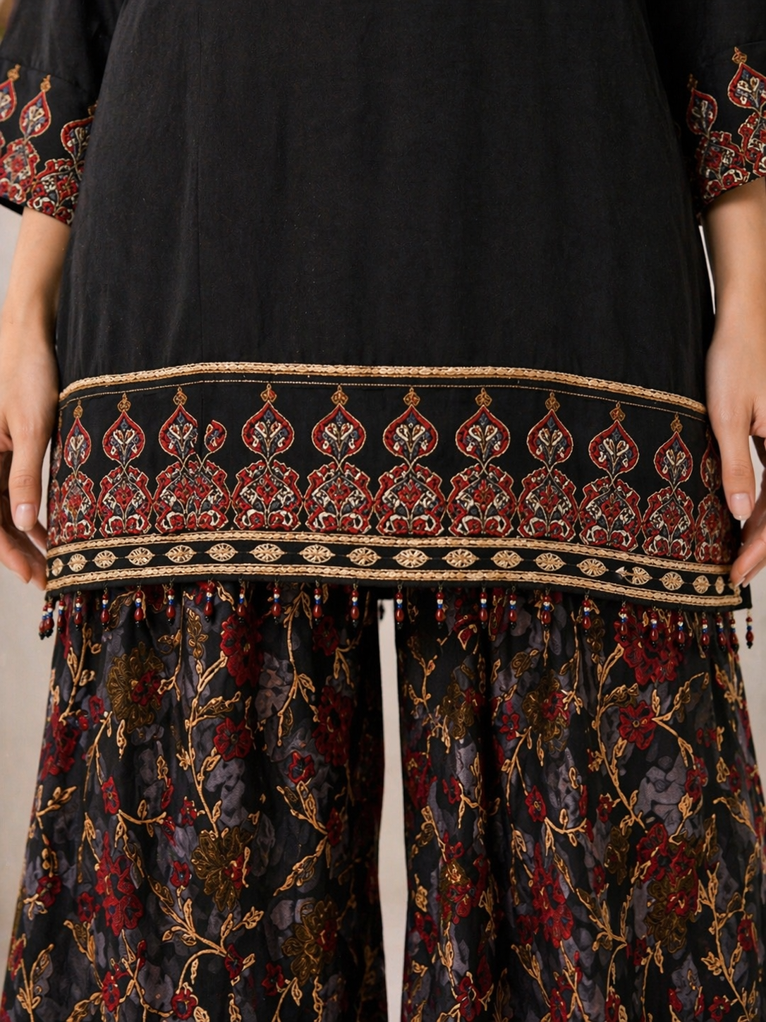 Detailed embroidered hem of black kurta with traditional border and tassel design